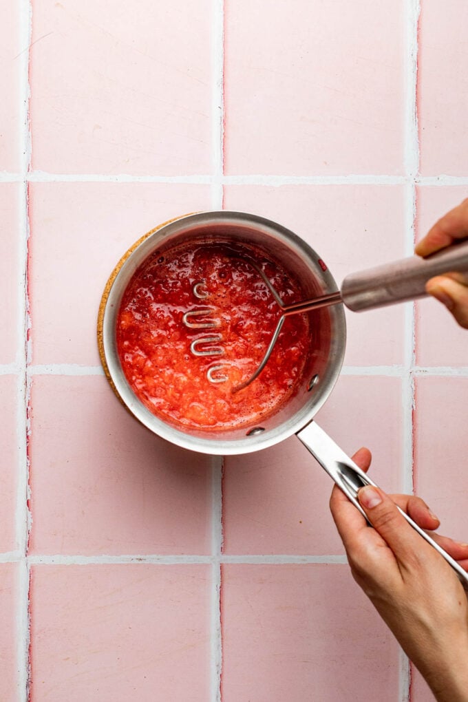 hand mashing strawberries in pot