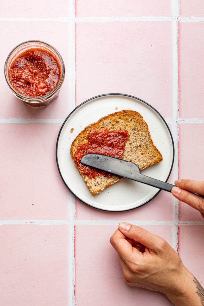 hand spreading chia jam on toast