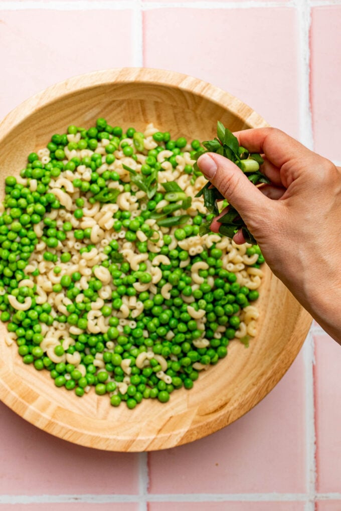 hand putting green onions in pasta bowl