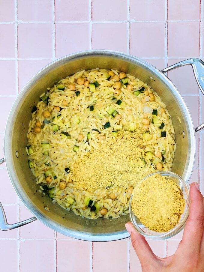 hand shaking nutritional yeast into pasta