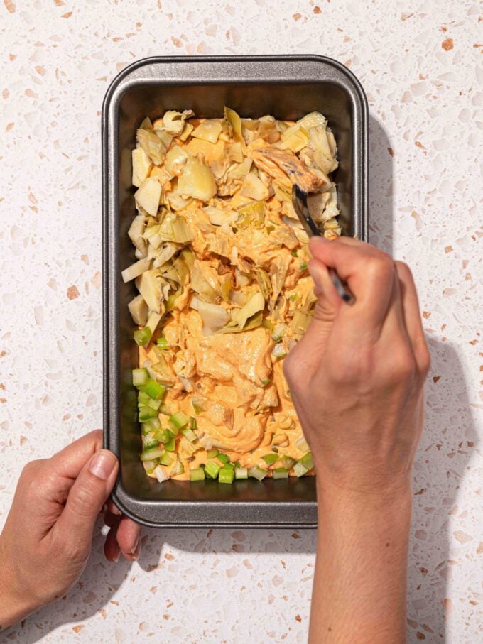 hand mixing artichokes into dip