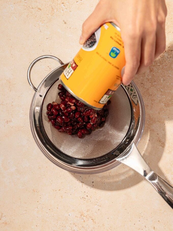 hand pouring black beans into strainer