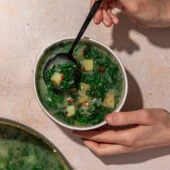 hands holding bowl of kale and potato soup