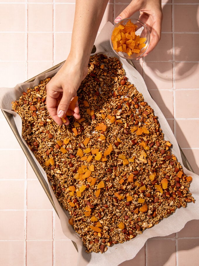 hand adding apricots to buckwheat granola