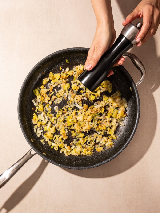 hand with pepper grinder and pan of leeks