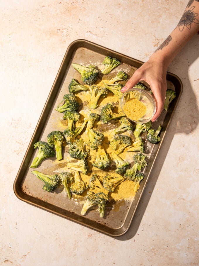 hand sprinkling nutritional yeast onto broccoli