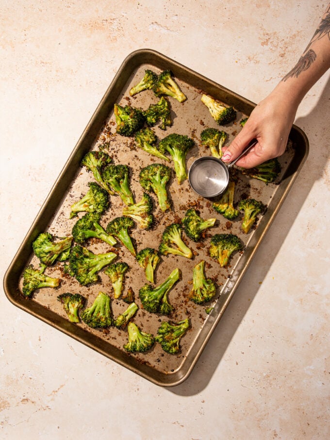 hand smashing broccoli on baking sheet