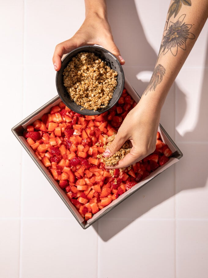 hand sprinkling crumble over strawberries