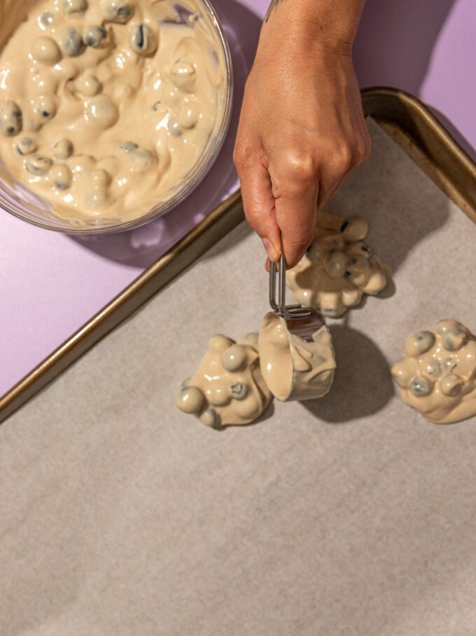 hand pouring blueberry yogurt clusters onto pan