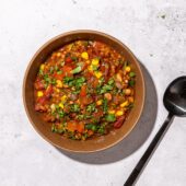 red lentil chili in brown bowl with black spoon