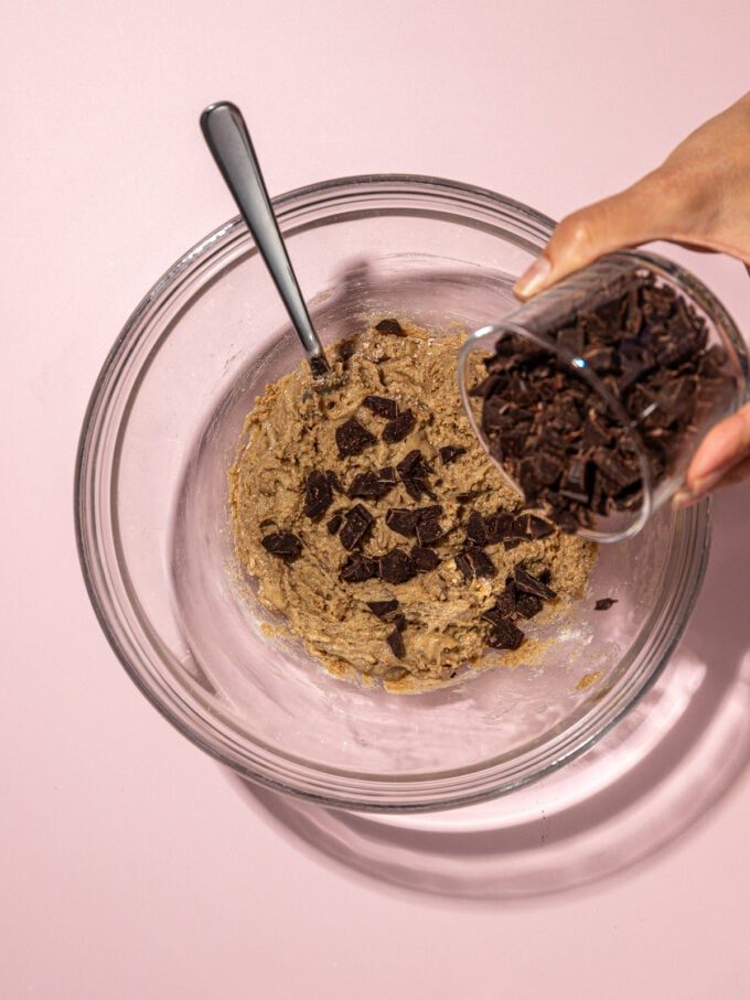 hand adding chocolate to cookie dough