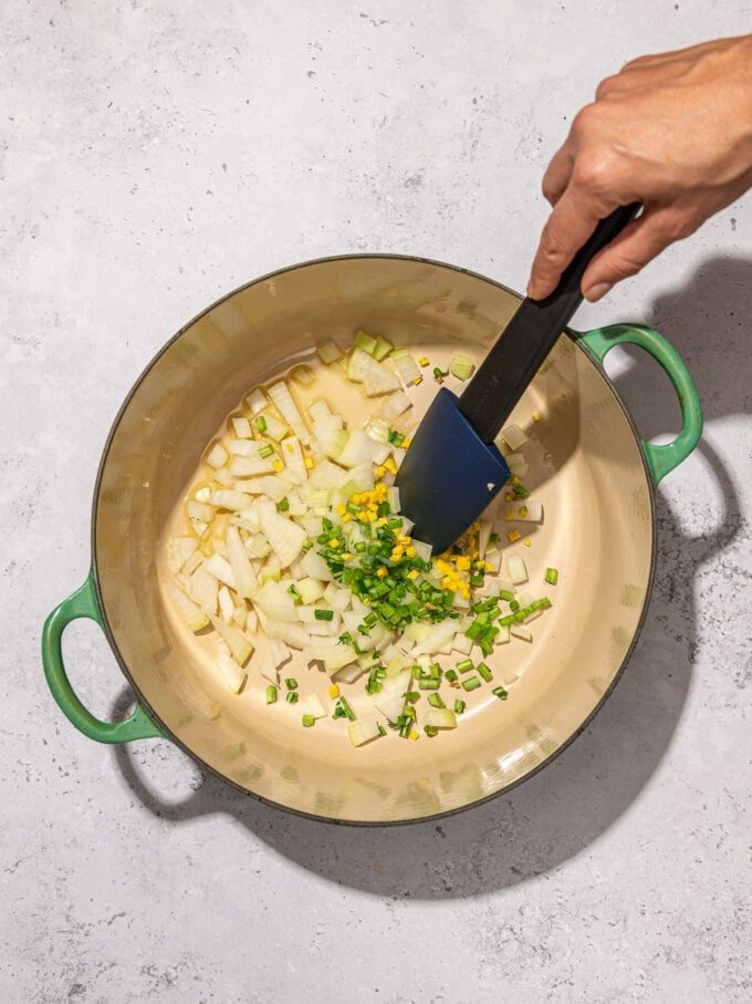 hand stirring onion and kale in pot