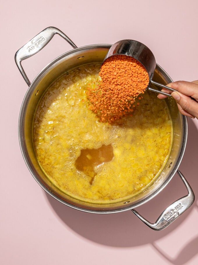 pouring red lentils into soup