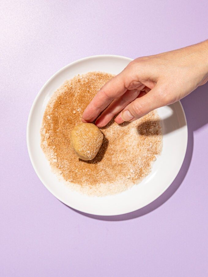 hand rolling cookie in cinnamon sugar