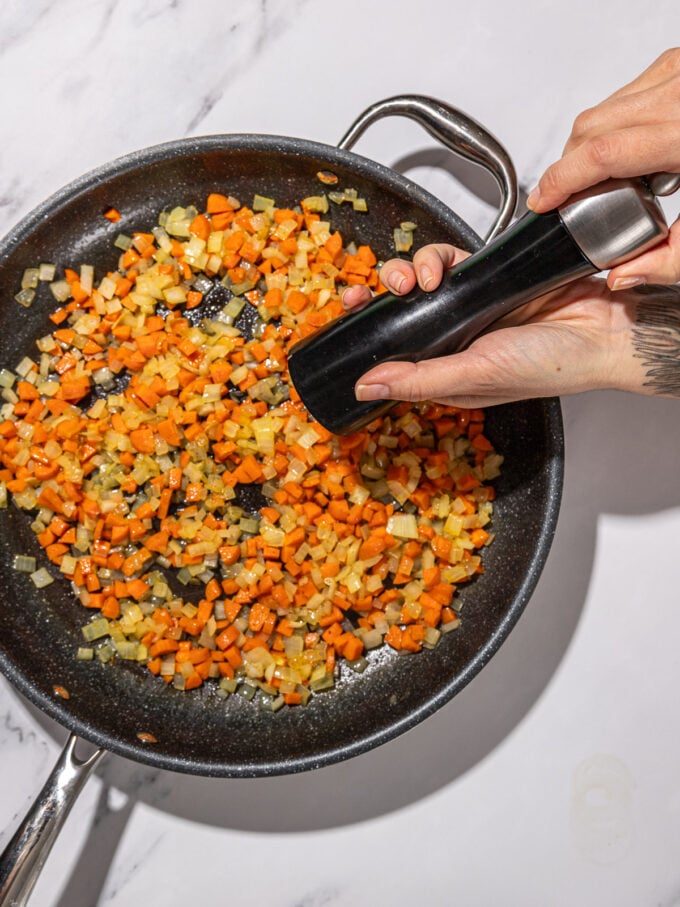 hand cracking pepper into carrots