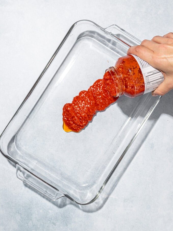 Hand pouring marinara sauce into pan