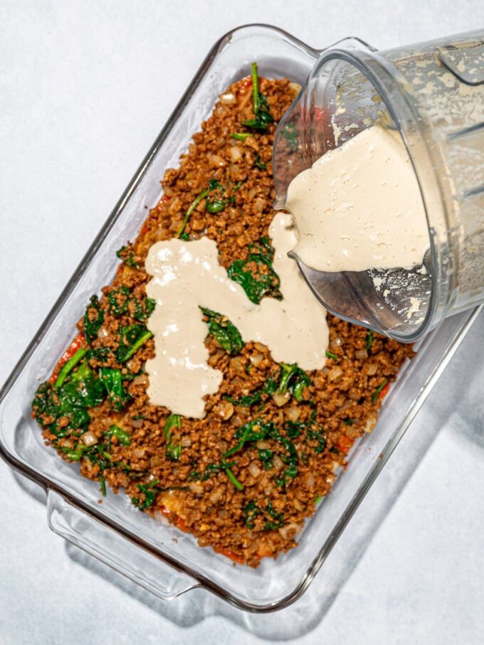 pouring cashew cream onto lasagna