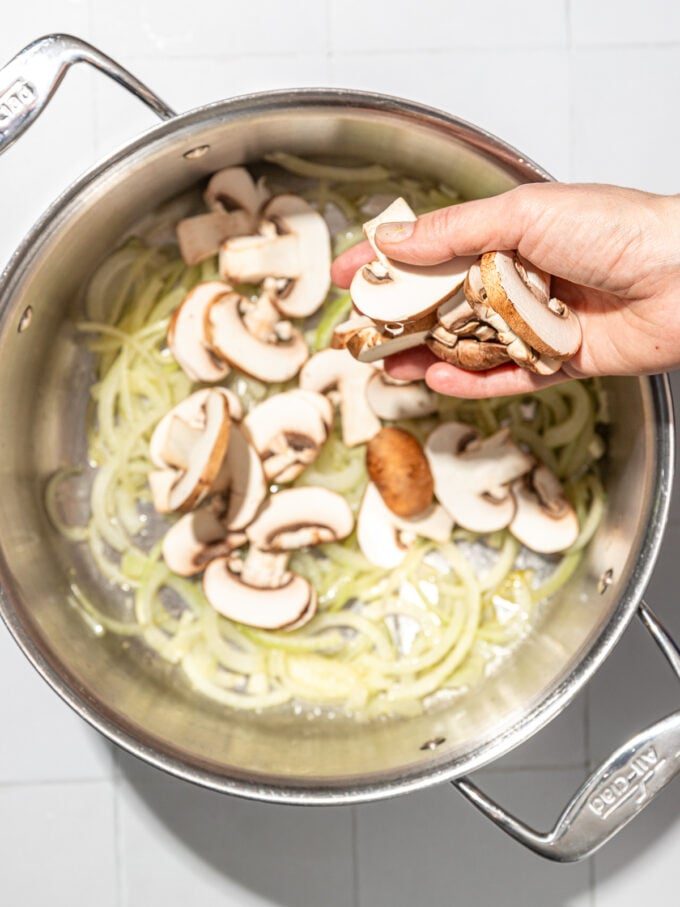 hand adding mushrooms to pot of onions