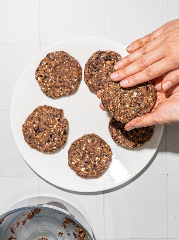 hand forming black bean burgers over white plate