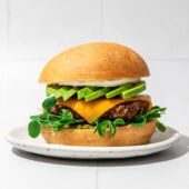 burger and bun on white plate with avocado and cheese