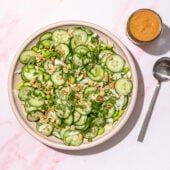 cucumber and peanut salad in a pink bowl with a jar of peanut sauce and spoon on the side