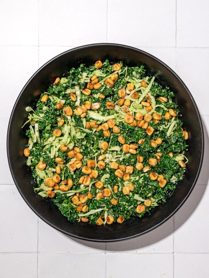 kale and cabbage salad with corn nuts in black bowl