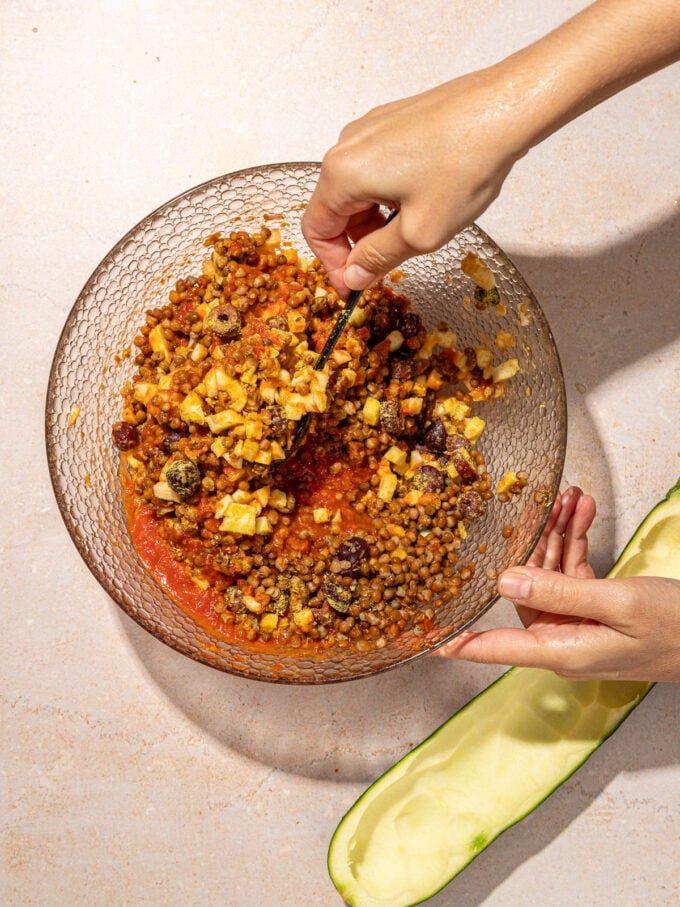 hand stirring lentil sauce in bowl