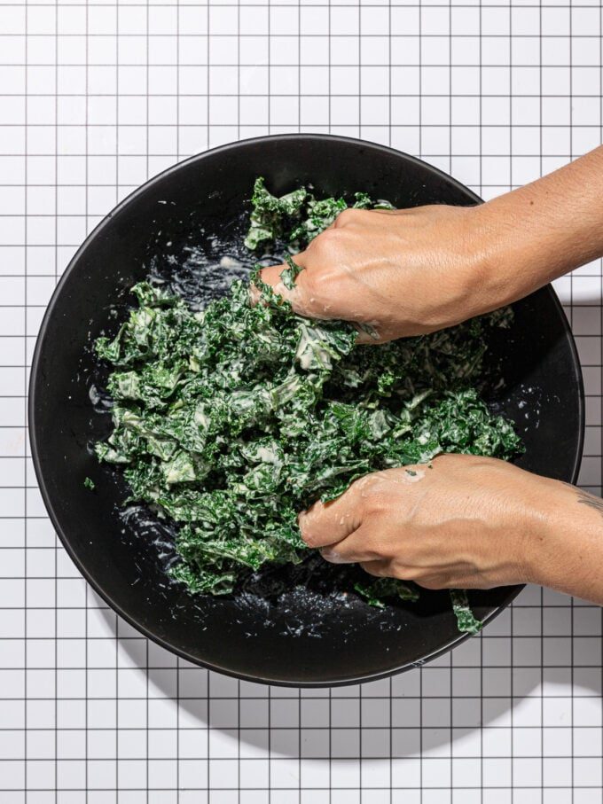 hands massaging kale in black bowl