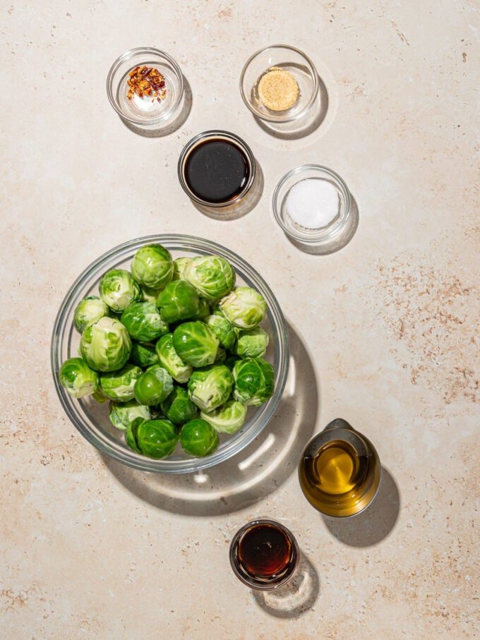 glass bowl of Brussels sprouts with bowls of maple syrup, balsamic vinegar and oil