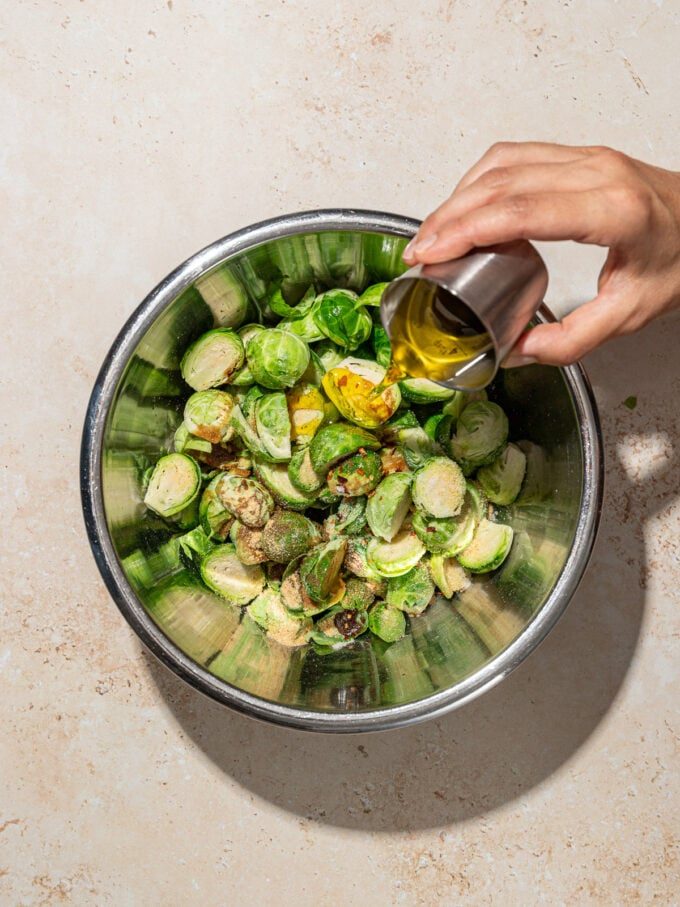 hand pouring oil onto brussels sprouts in metal bowl