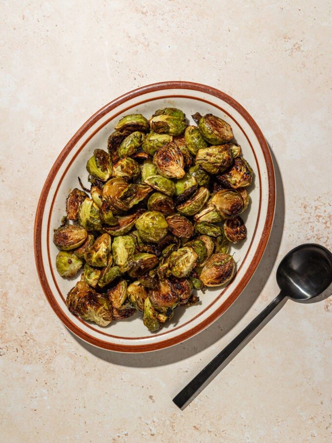 roasted brussels sprouts on a brown plate with black spoon
