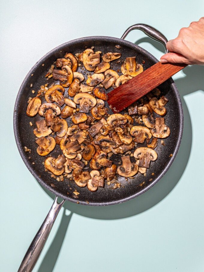 hand stirring mushrooms in skillet