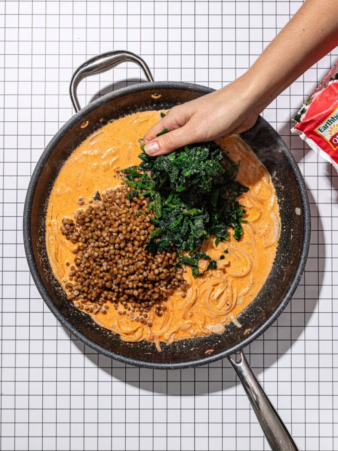 hand adding spinach to curry lentils