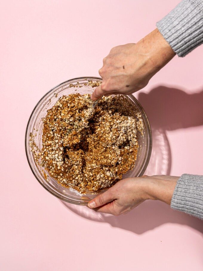 hand stirring monster cookie dough with a fork on pink background