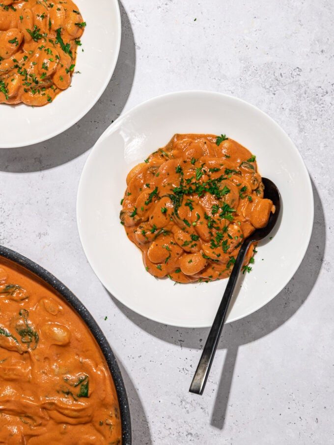 butter beans in creamy rose sauce in white bowls with black spoon