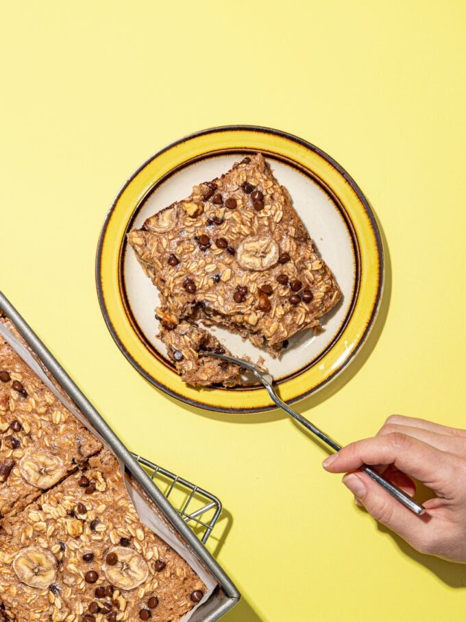 hand cutting piece of banana baked oats with fork on yellow rimmed plate