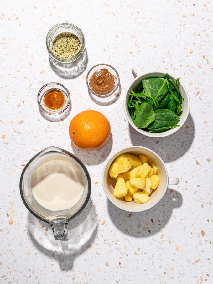bowls of soy milk, spinach, pineapple and an orange