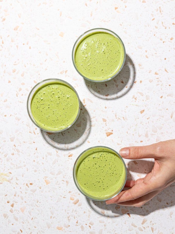 three glasses of green smoothies and hand holding glass