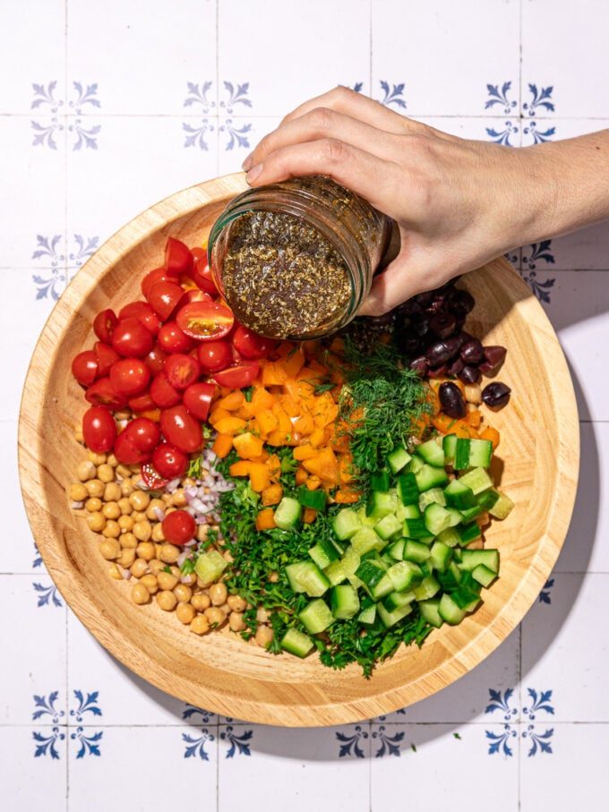 hand pouring dressing over greek salad with chickpeas