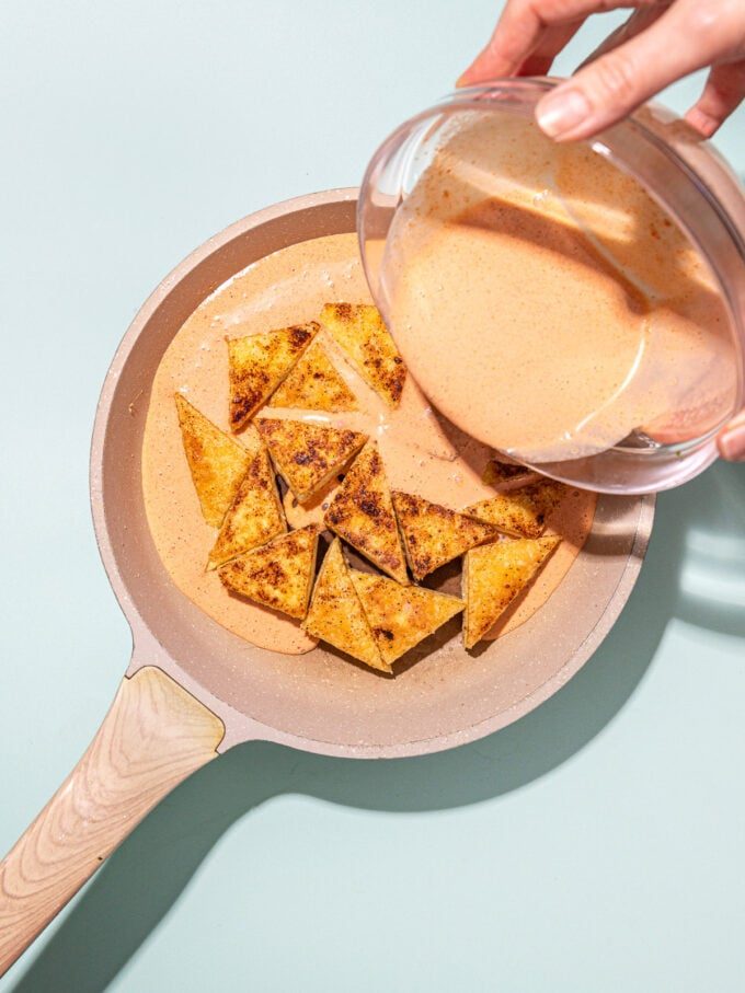 pouring creamy sauce onto tofu in skillet