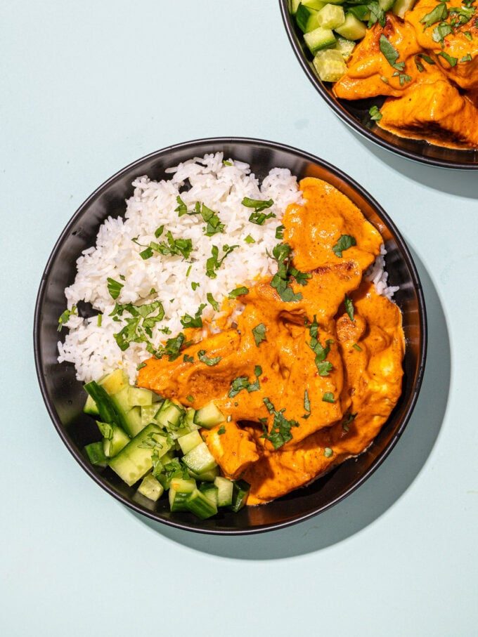 tofu with a sauce, white rice and cucumber in a black bowl