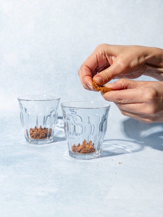 hand crumbling biscoff cookies into dessert glasses