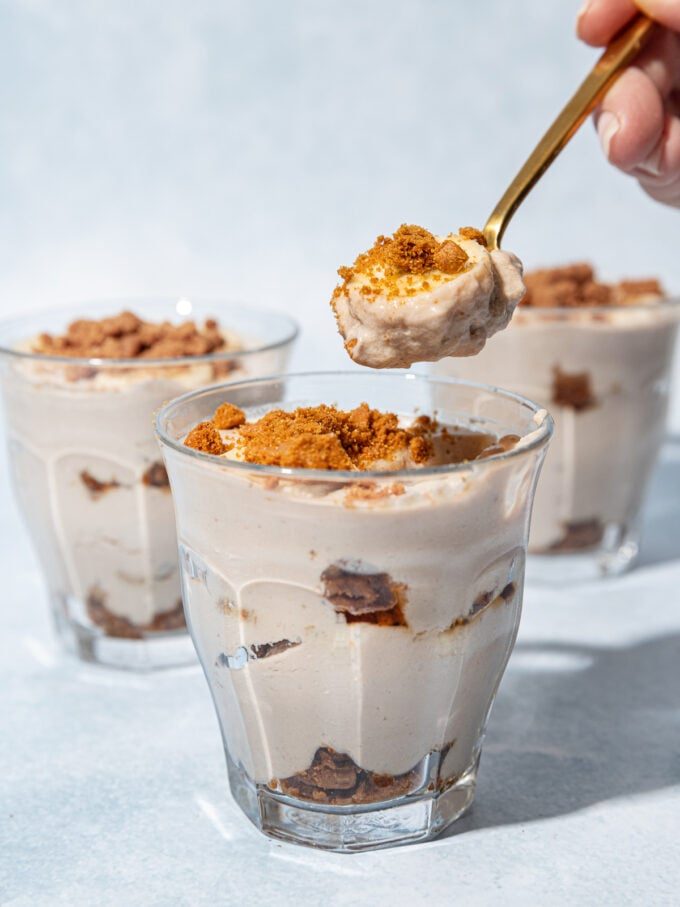 hand holding a spoonful of banana biscoff pudding with dessert glasses