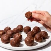 hand holding chocolate protein ball above plate of balls