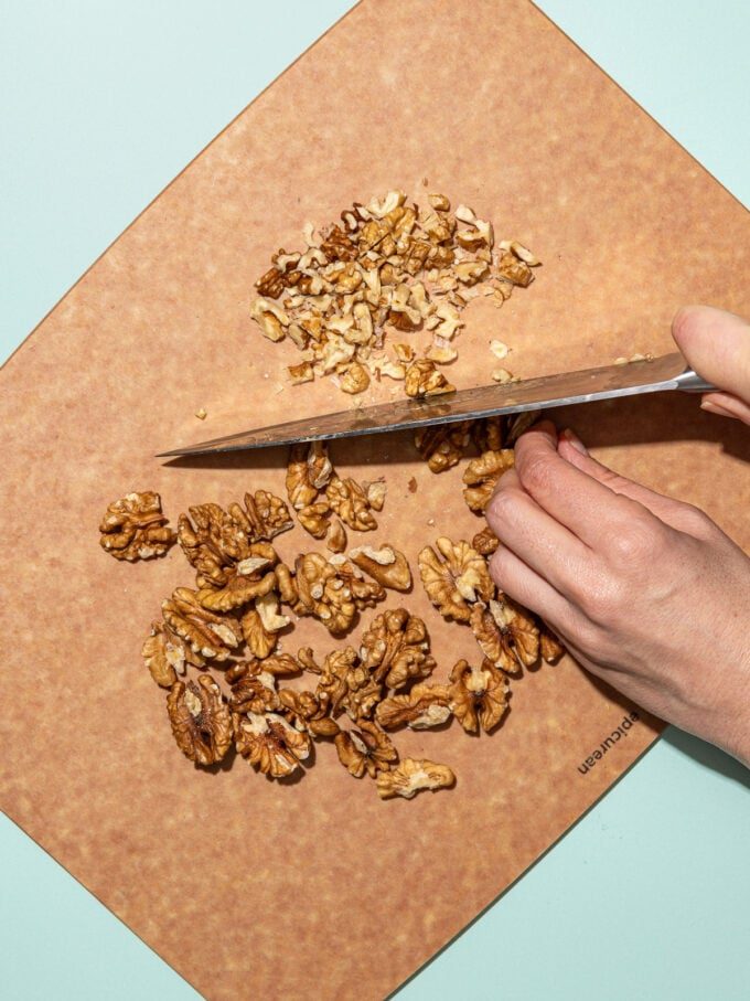 hand chopping walnuts on a wood cutting board