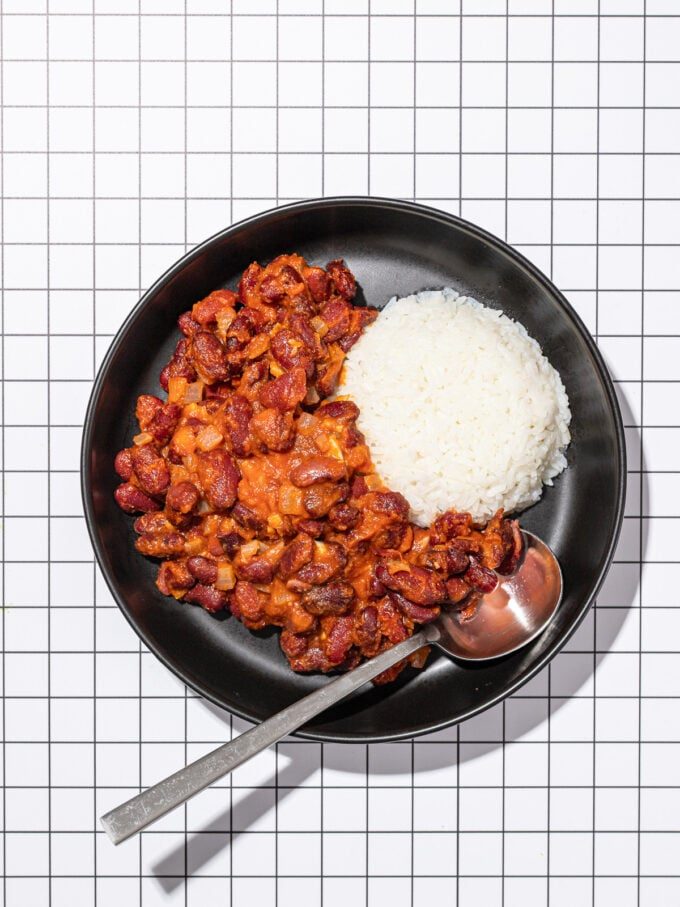 saucy kidney beans with white rice in black bowl with spoon