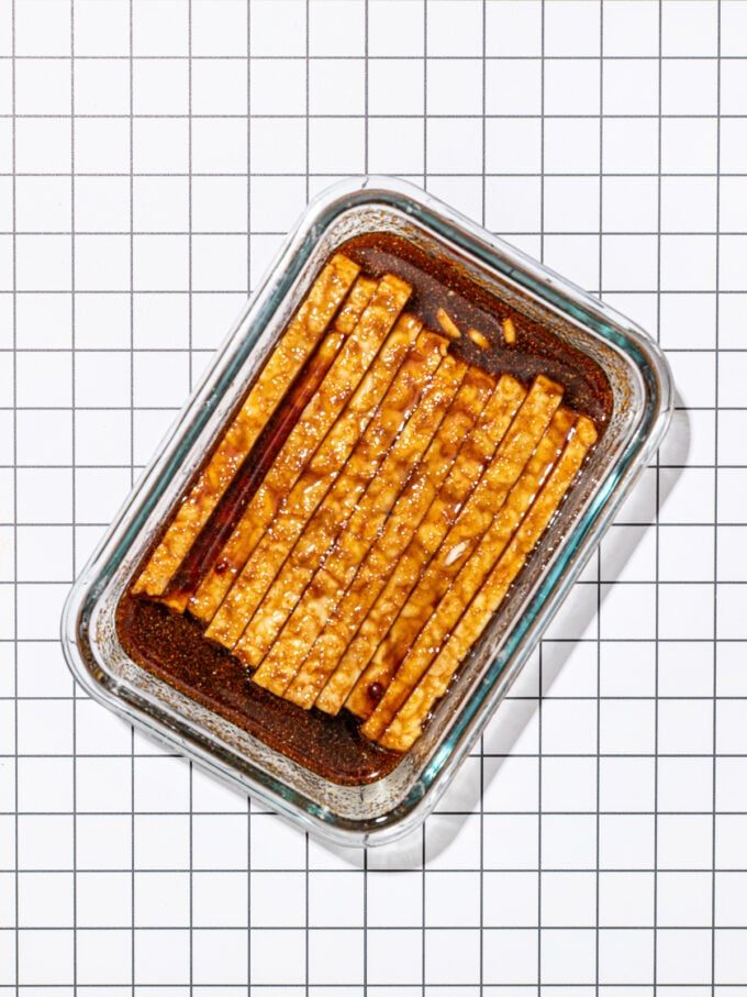 sliced tempeh in marinade in glass container