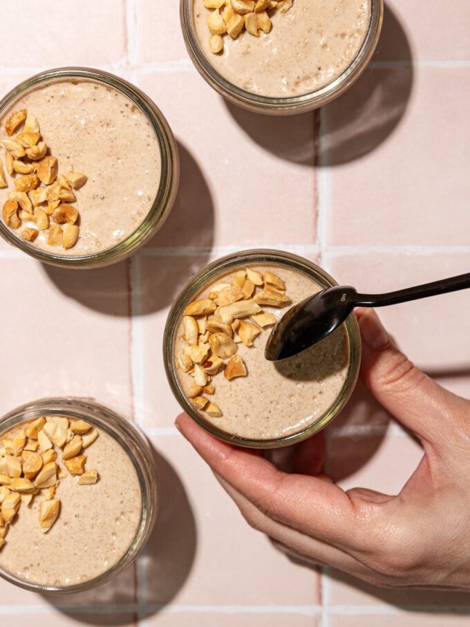 black spoon dipping into glass jars of blended chia pudding with crushed peanuts