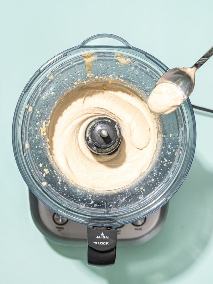 spoon with scoop of whipped tahini next to food processor
