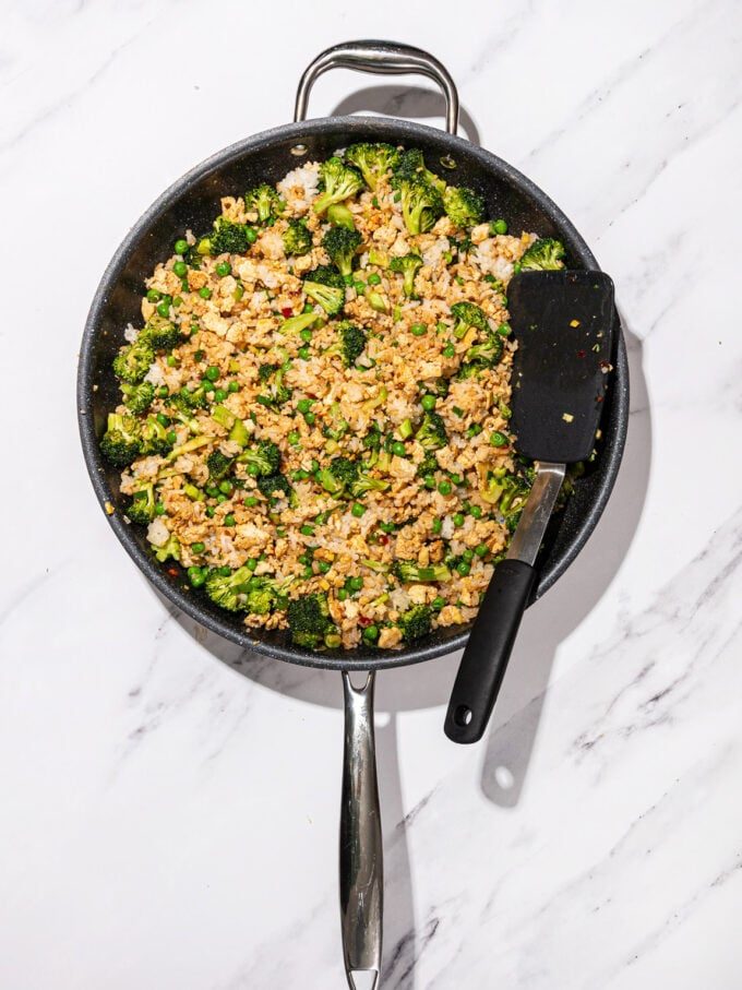 skillet with tofu fried rice with broccoli and peas and a black spatula